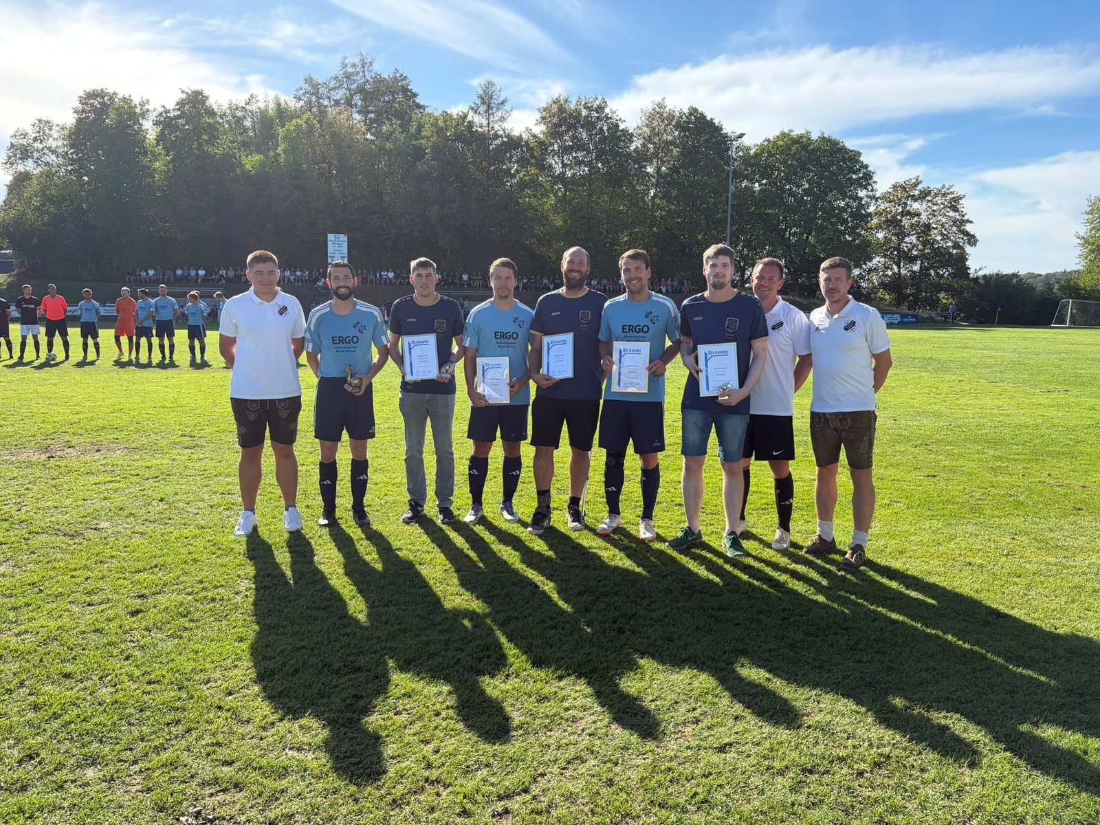 Geehrte Spieler mit Urkunden zwischen Vorstandsmitgliedern auf dem Sportplatz