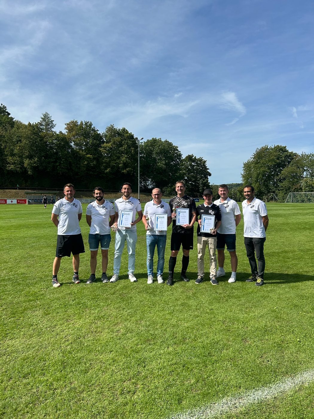 Geehrte Vereinsmitglieder mit Urkunden und Pokalen auf dem Sportplatz in Niederhofen