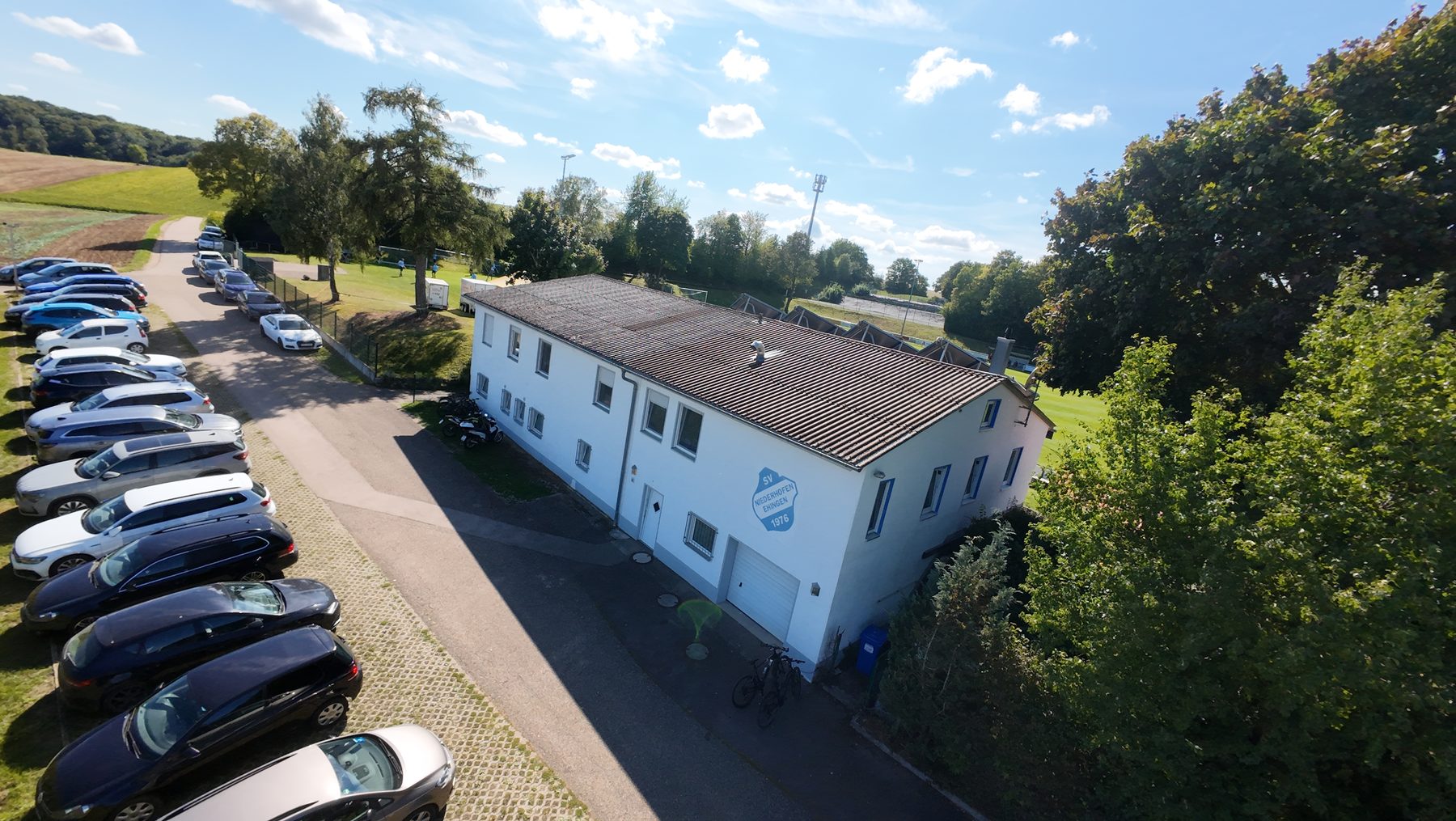 Luftaufnahme des Sportheims Niederhofen mit Vereinswappen an der frisch gestrichenen Fassade und Parkplatz