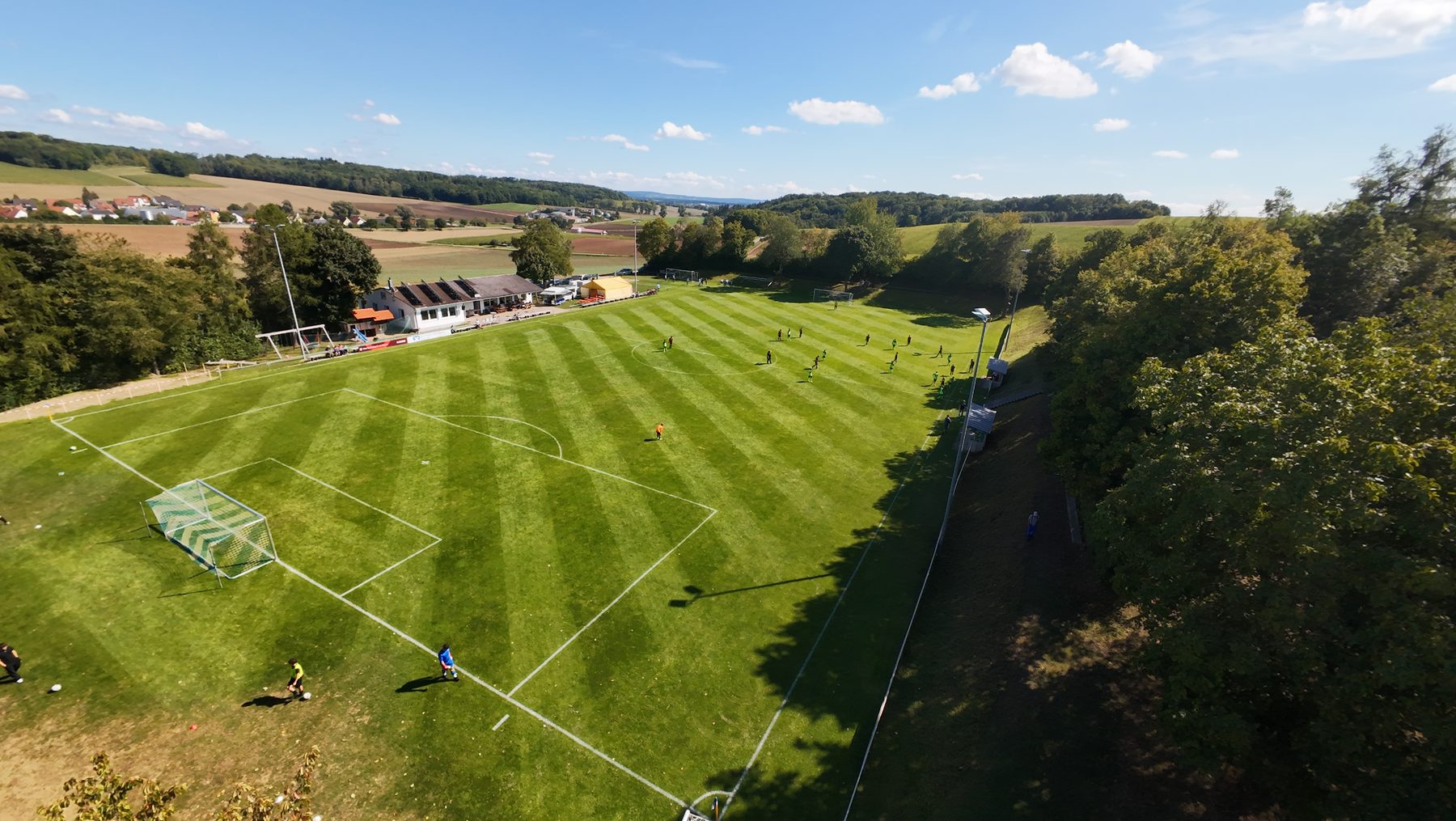 Luftaufnahme des Sportplatzes Niederhofen mit frisch gemähtem Rasen, Sportheim und umliegenden Bäumen